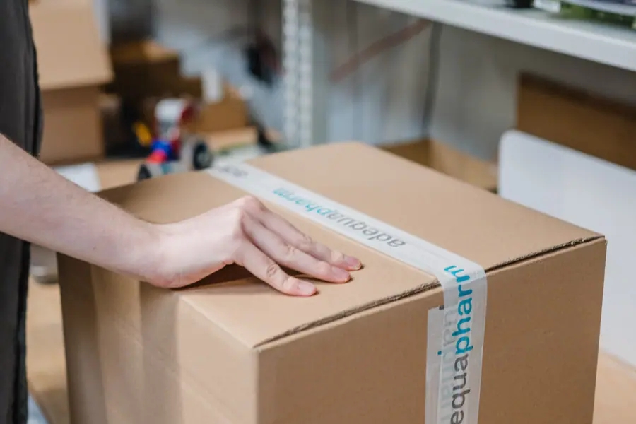Eine Hand auf einem adequapharm-Karton am Packtisch